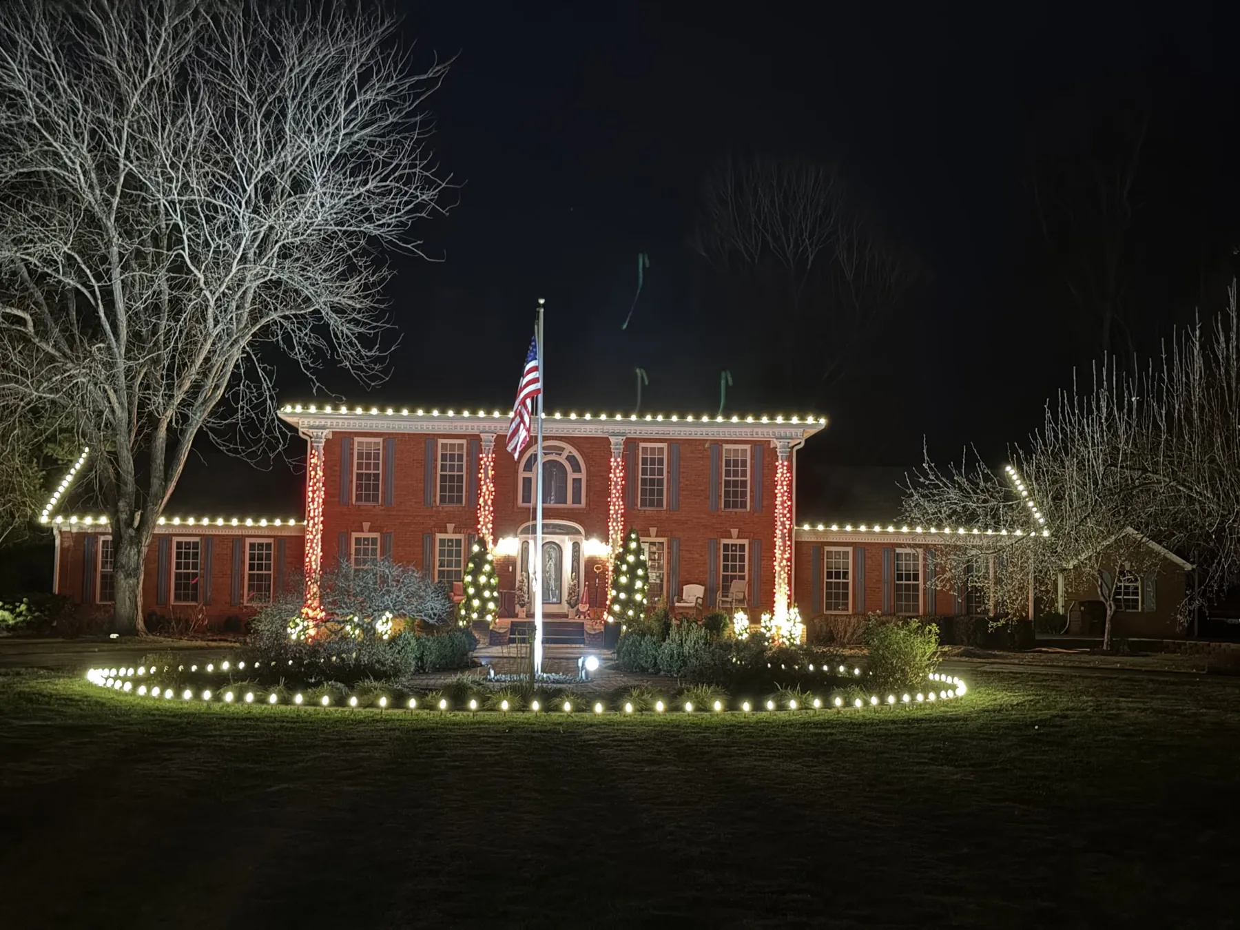Brick colonial home lit by Prestige: white roofline, wrapped columns and a lit circle drive, December 2025